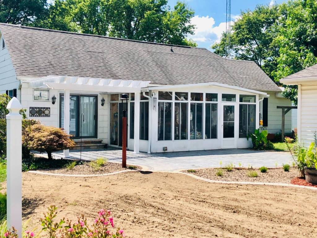 Completed backyard patio and white pergola beside a residential sunroom