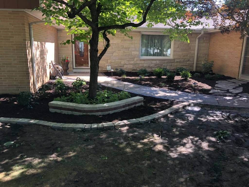 Landscaped residential courtyard with fresh mulch, shrubs, stone edging, and walkway
