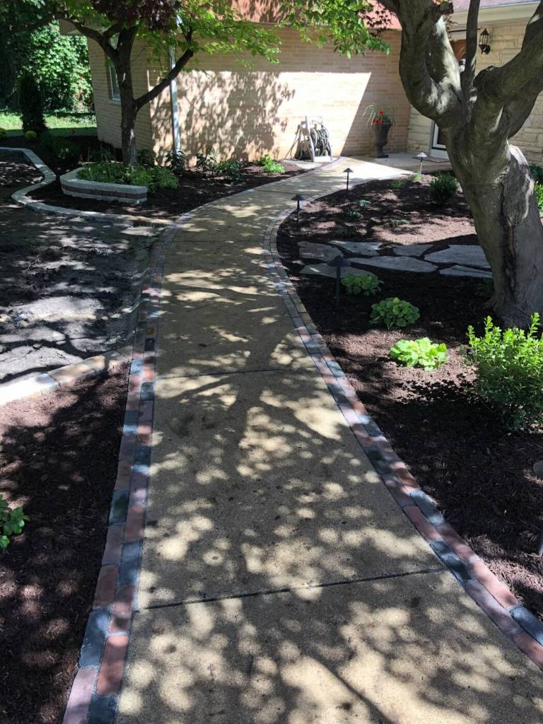 Curved residential walkway bordered by fresh mulch, plants, stone accents, and landscape lighting