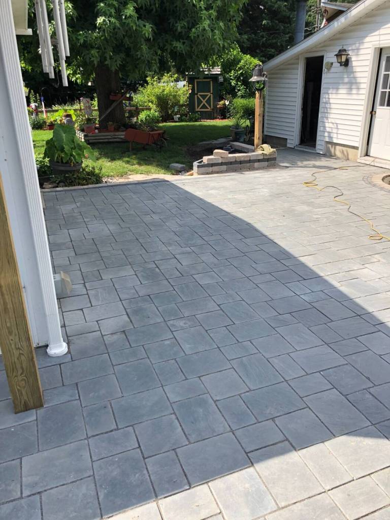 Large gray paver patio installed between a home and detached garage