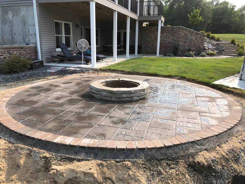 Circular stamped concrete patio with brick edging and a central stone fire pit