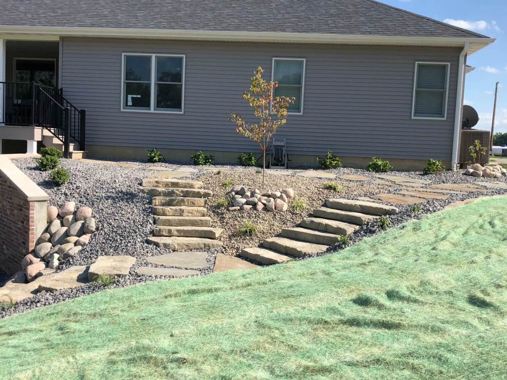 Finished residential rock landscape with natural stone steps, young trees, and planted beds