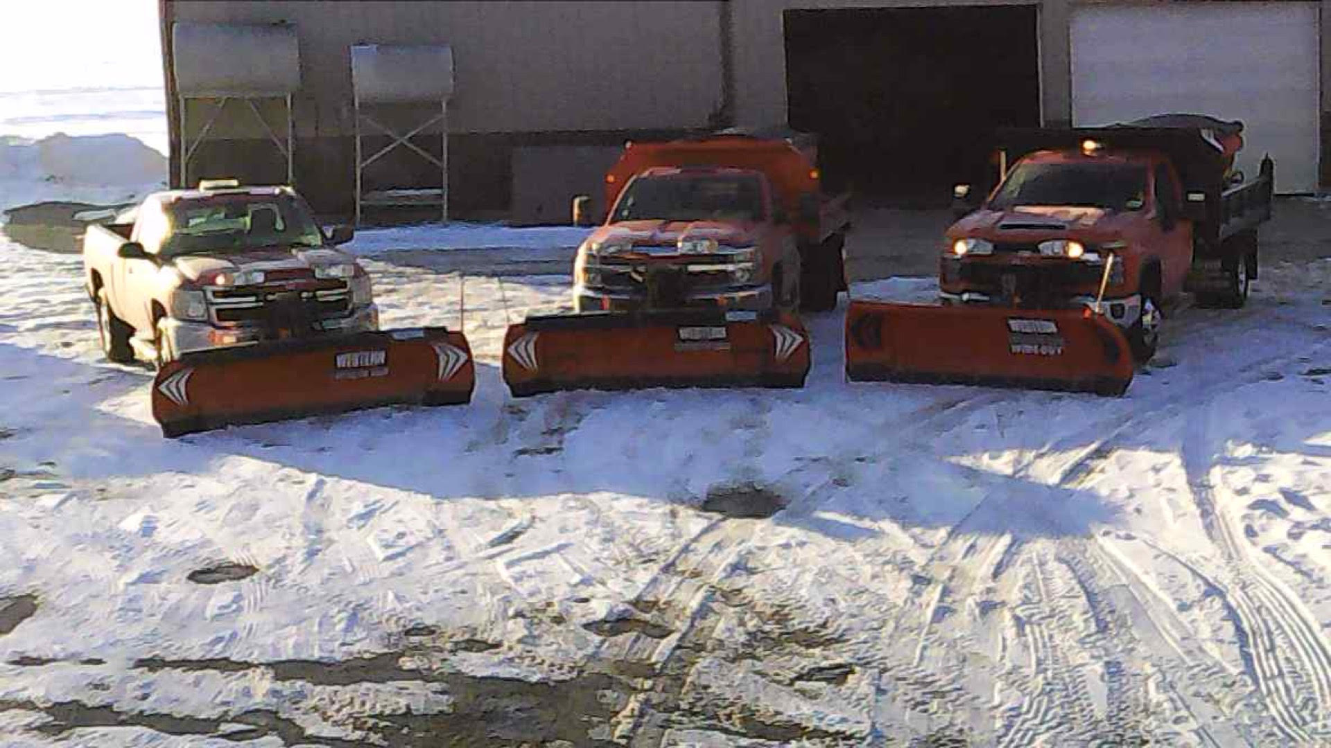 Three snowplow trucks parked in a snowy lot